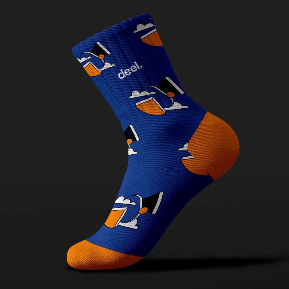 Design As A Service 24 Blue sock with an orange heel and toe, featuring a cartoon graphic of a person with a hat and sunglasses against a dark background. The word deel. is printed near the top, showcasing unlimited graphic design creativity.